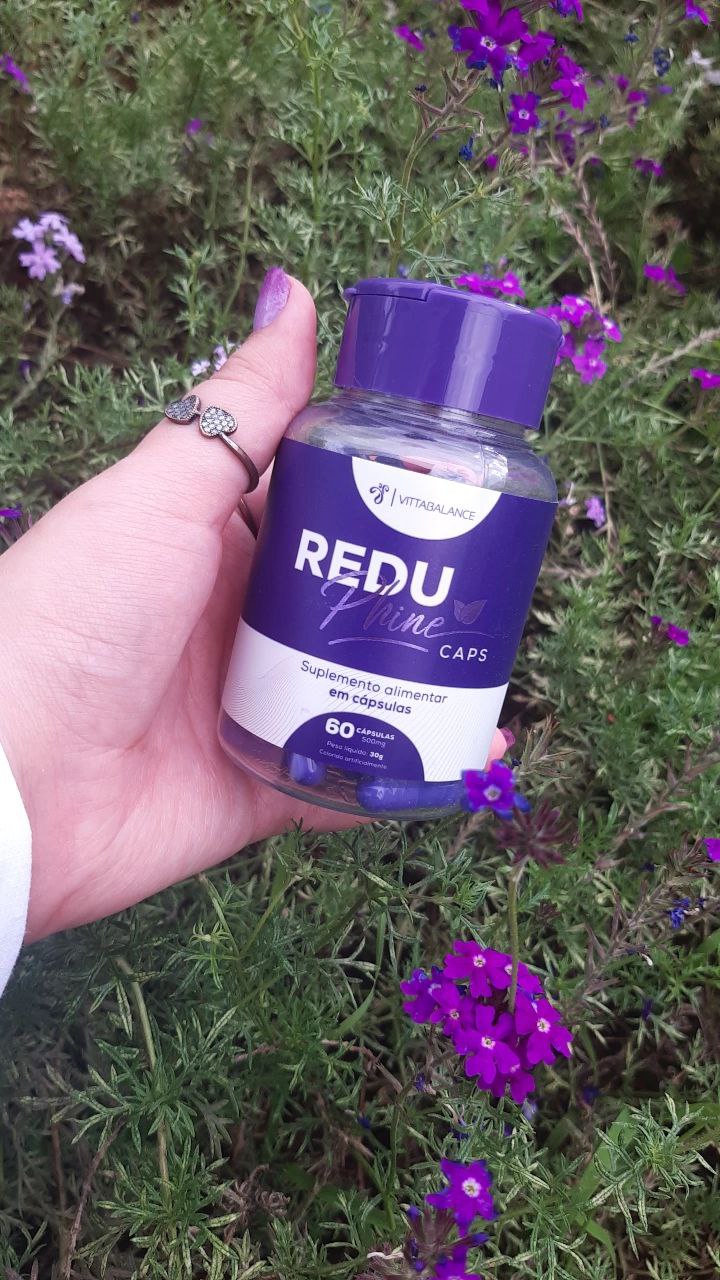 Um frasco de ReduPhine Caps na mão com fundo de flores roxas