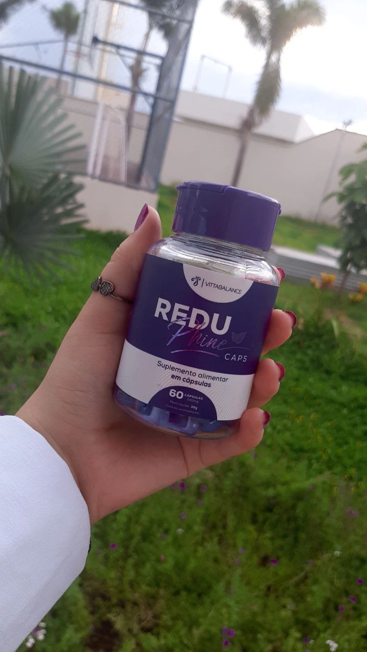 Frasco do ReduPhine Caps na mão com fundo de jardim florido